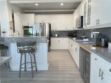 Kitchen featuring white cabinets, a kitchen breakfast bar, beverage cooler, glass insert cabinets, and appliances with stainless steel finishes