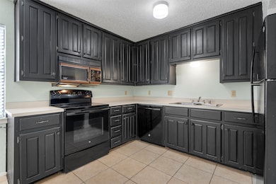 Kitchen featuring black appliances, light countertops, light tile patterned floors, a textured ceiling, and dark cabinets