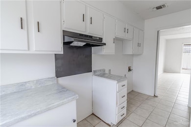 Kitchen with white cabinetry and light tile patterned floors with view to dining/livingroom.