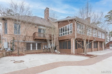 Rear view of house featuring a sunroom, a chimney, brick siding, and a balcony