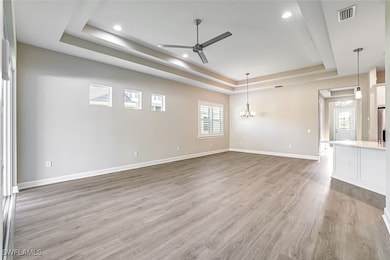 Unfurnished living room featuring a tray ceiling, light wood finished floors, ceiling fan, and a chandelier
