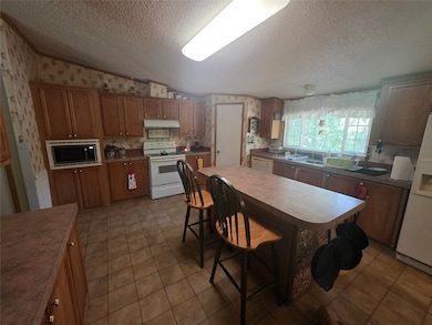 Kitchen with wallpapered walls, white appliances, brown cabinetry, a breakfast bar area, and a textured ceiling