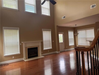 Unfurnished living room with a high ceiling, ceiling fan, baseboards, wood finished floors, and a glass covered fireplace
