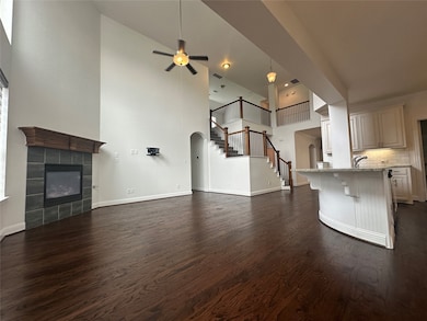 Unfurnished living room with dark wood-style floors, a towering ceiling, stairs, a tiled fireplace, and a ceiling fan