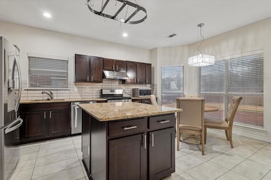 Kitchen with dark brown cabinetry, light stone cou