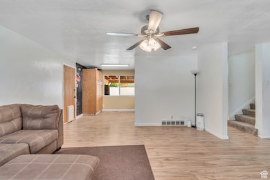 Living room with light wood finished floors, ceiling fan, and stairway
