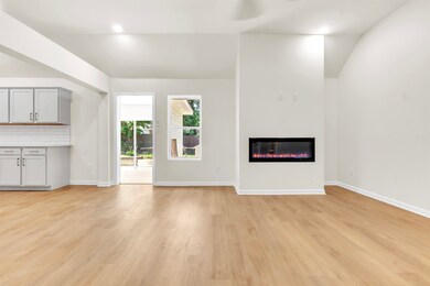 Unfurnished living room featuring vaulted ceiling, a glass covered fireplace, light wood-style flooring, and baseboards