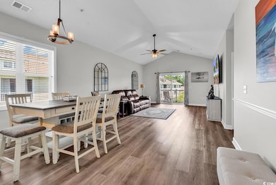 Dining space with vaulted ceiling, wood finished floors, a ceiling fan, and a chandelier