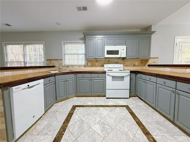 Kitchen featuring gray cabinetry, inlaid floor details, white appliances, a peninsula, and recessed lighting