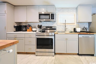 Kitchen with butcher block counters, stainless steel appliances, tasteful backsplash, light marble finish flooring, and white cabinets