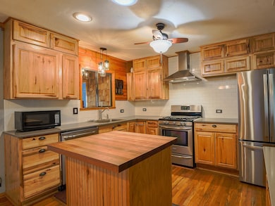 Kitchen featuring stainless steel appliances, decorative backsplash, decorative light fixtures, wall chimney range hood, and dark wood-style floors