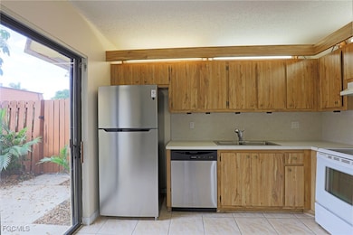 Kitchen featuring light countertops, stainless steel appliances, a textured ceiling, brown cabinetry, and light tile patterned floors