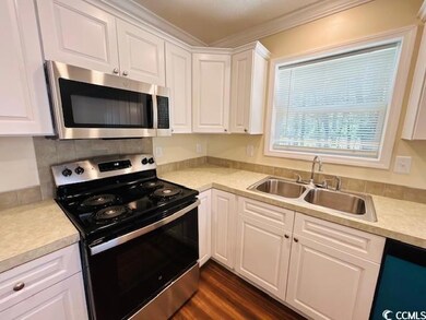 Kitchen with stainless steel appliances, a sink, white cabinets, light countertops, and ornamental molding