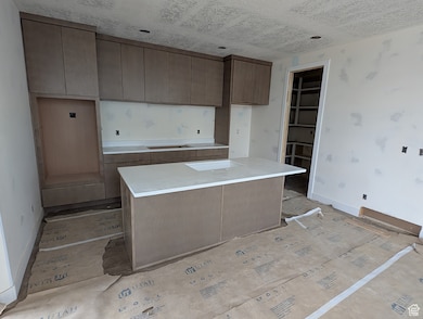 Kitchen featuring a kitchen island with sink, brown cabinets, modern cabinets, light stone countertops, and black electric cooktop