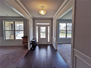 Foyer with ornamental molding, a decorative wall, a wainscoted wall, dark colored carpet, and dark wood-style flooring