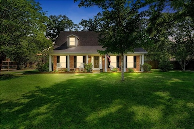 View of front facade featuring covered porch, brick siding, fence, and a front lawn