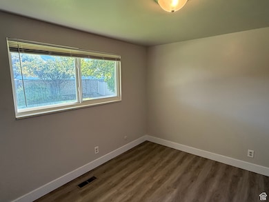 Spare room featuring baseboards and dark wood-type flooring