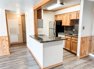 Kitchen featuring wooden walls, a wainscoted wall, tasteful backsplash, dark stone counters, and a peninsula