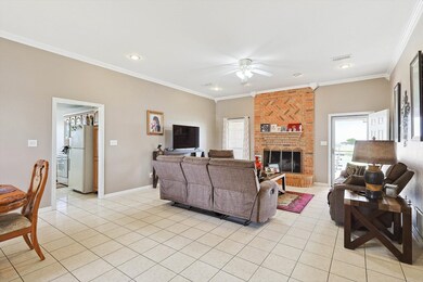 Living room with a fireplace, brick wall, light tile patterned floors, and ceiling fan