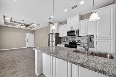 Kitchen featuring appliances with stainless steel finishes, tasteful backsplash, white cabinetry, light wood-style flooring, and a tray ceiling