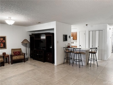 Living area with light tile patterned floors, visible vents, a textured ceiling, and baseboards