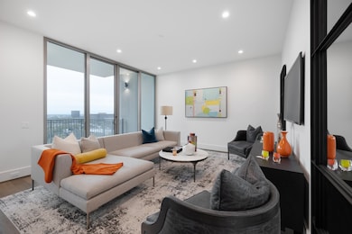 Open living space with expansive floor-to-ceiling windows, providing abundant natural light and sweeping views of the city. The spacious layout features clean architectural lines, recessed lighting, and direct access to a private balcony. (Sample of another model)