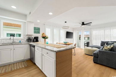 Kitchen featuring open floor plan, dishwasher, a peninsula, white cabinets, and light wood-style flooring