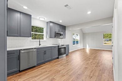 Kitchen featuring gray cabinets, appliances with stainless steel finishes, backsplash, light wood-style floors, and lofted ceiling