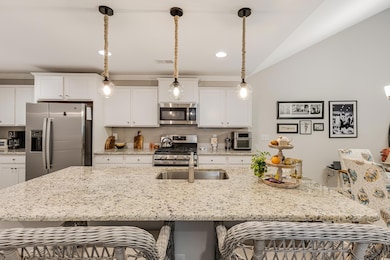 Kitchen with appliances with stainless steel finishes, a breakfast bar, white cabinets, pendant lighting, and vaulted ceiling