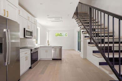 Kitchen with tasteful backsplash, baseboards, light wood-style flooring, stainless steel appliances, and a sink