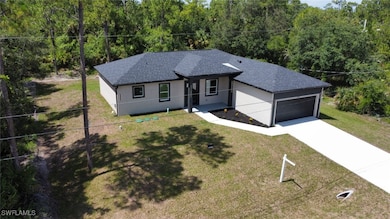 Ranch-style house featuring a shingled roof, a garage, driveway, a wooded view, and stucco siding