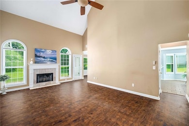 Unfurnished living room featuring high vaulted ceiling, ceiling fan, baseboards, wood finished floors, and a tiled fireplace