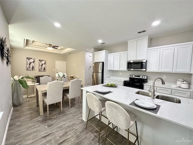 Kitchen with stainless steel appliances, a breakfast bar area, white cabinetry, a raised ceiling, and light wood-style floors