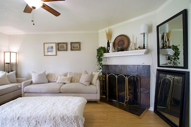 Living area with a textured ceiling, wood finished floors, ornamental molding, a ceiling fan, and a fireplace