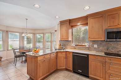 Kitchen featuring light stone counters, a peninsula, brown cabinetry, black appliances, and backsplash