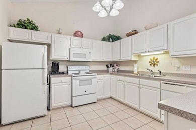 Kitchen featuring white appliances, white cabinetry, light tile patterned floors, and a chandelier