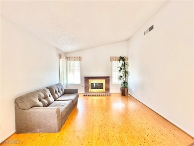 Living room with hardwood / wood-style floors, a brick fireplace, a textured ceiling, and lofted ceiling