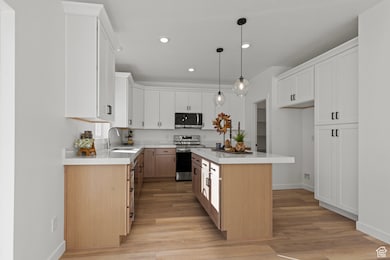 Kitchen with a kitchen island, white cabinets, pendant lighting, appliances with stainless steel finishes, and recessed lighting.