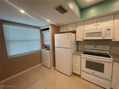 Kitchen with backsplash, stacked washer / dryer, white appliances, and white cabinetry