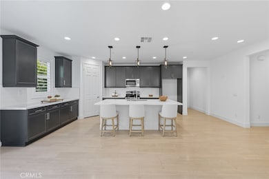 Sleek and spacious kitchen featuring an oversized island with seating, quartz countertops, stainless steel appliances, ample cabinetry, recessed lighting, and luxury laminate wood flooring, perfectly blending style and functionality