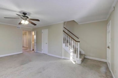 Unfurnished living room featuring stairway, ornamental molding, light carpet, and ceiling fan