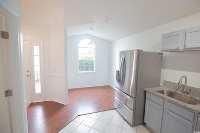 Kitchen featuring a sink, vaulted ceiling, light wood-type flooring, stainless steel fridge with ice dispenser, and light stone counters