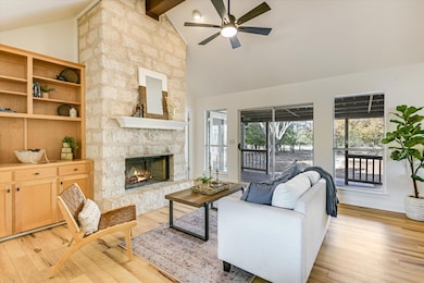 Living area with high vaulted ceiling, beam ceiling, a ceiling fan, light wood-style floors, and a stone fireplace