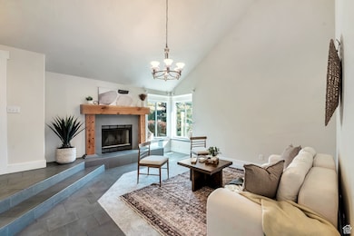 Living room with high vaulted ceiling, dark tile patterned floors, a fireplace, and a chandelier