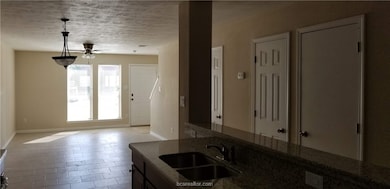 Kitchen with a textured ceiling, hanging light fixtures, dark stone counters, and ceiling fan