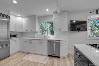 Kitchen with white cabinets, light stone counters, stainless steel appliances, decorative backsplash, and light wood-style floors