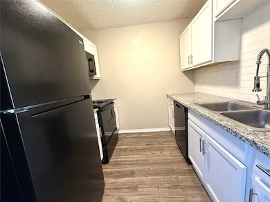 Kitchen featuring black appliances, dark wood-style floors, white cabinets, a textured ceiling, and tasteful backsplash