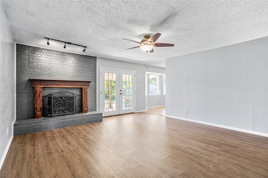 Unfurnished living room featuring a brick fireplace, a textured ceiling, wood finished floors, rail lighting, and ceiling fan