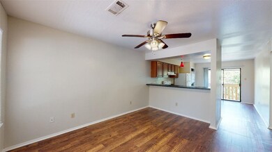 Kitchen with dark wood-type flooring, a ceiling fan, a peninsula, brown cabinetry, and freestanding refrigerator