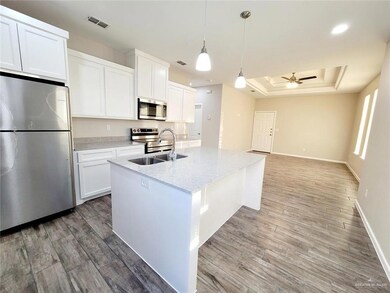 Kitchen with appliances with stainless steel finishes, a tray ceiling, a kitchen island with sink, light wood finished floors, and a ceiling fan